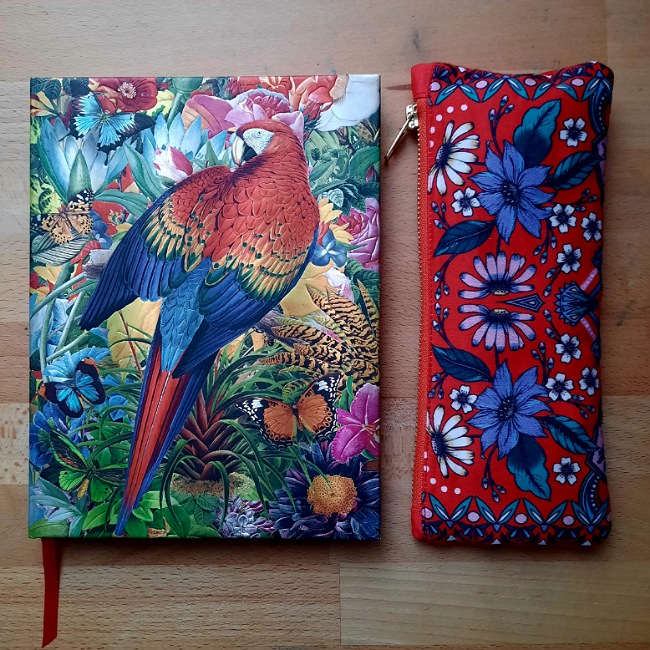 Buntes Notizbuch mit einem Papagei, Schüttelpenal in rot mit Blumen darauf.